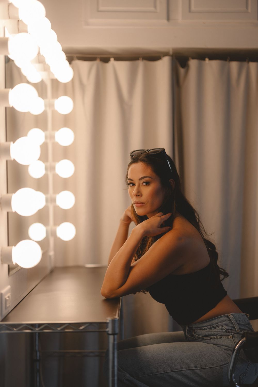 Moody portrait in a dressing room featuring dramatic vanity lighting and vintage aesthetic styling.
