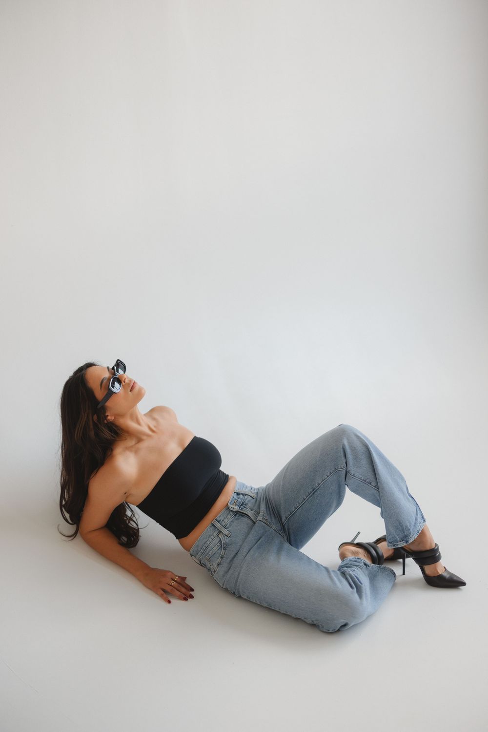 A person in black top and jeans reclines on white floor, captured in a series of four shifting poses.