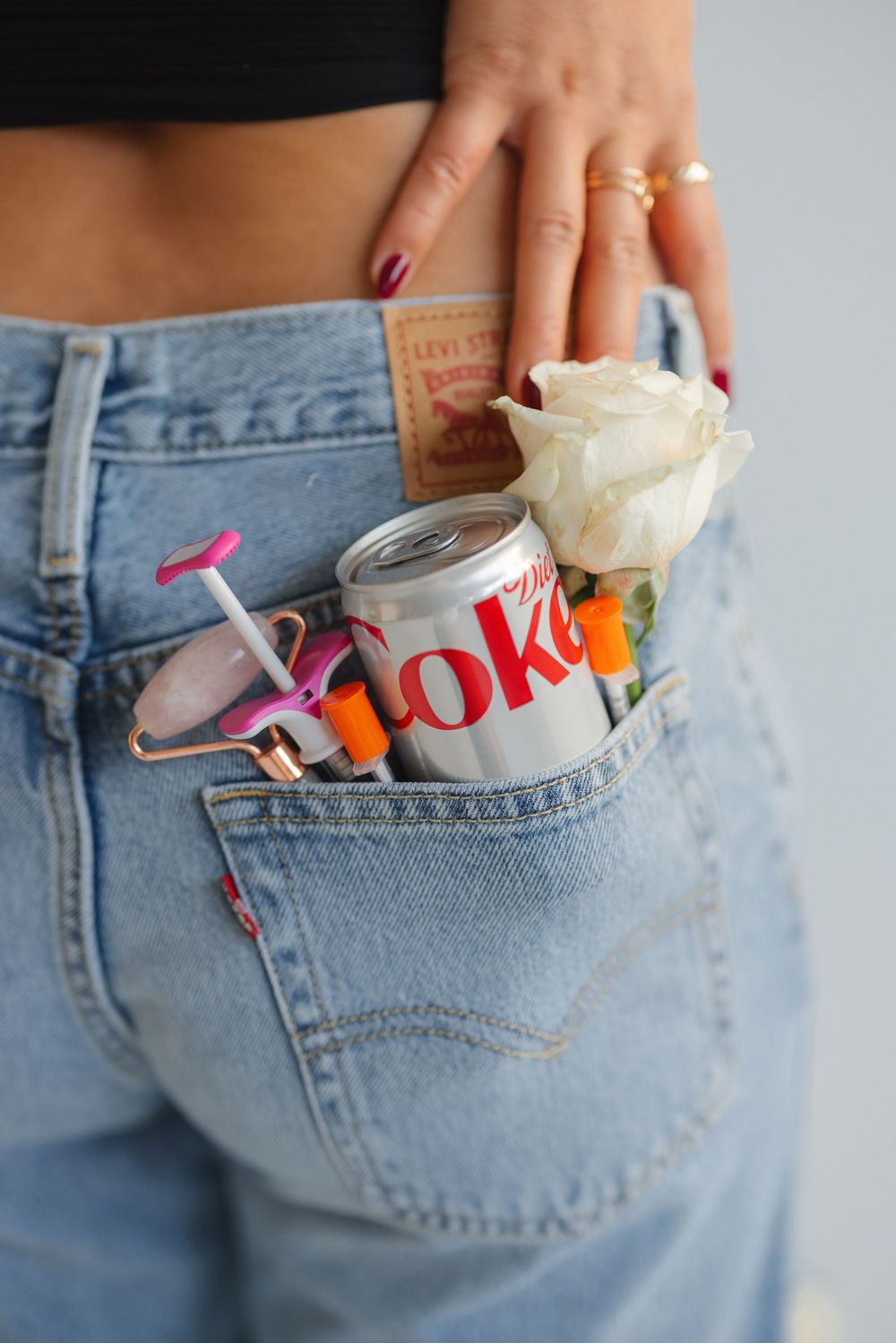 Hand placing everyday items including keys, lip balm, and a small bottle into a back pocket of light wash denim jeans.