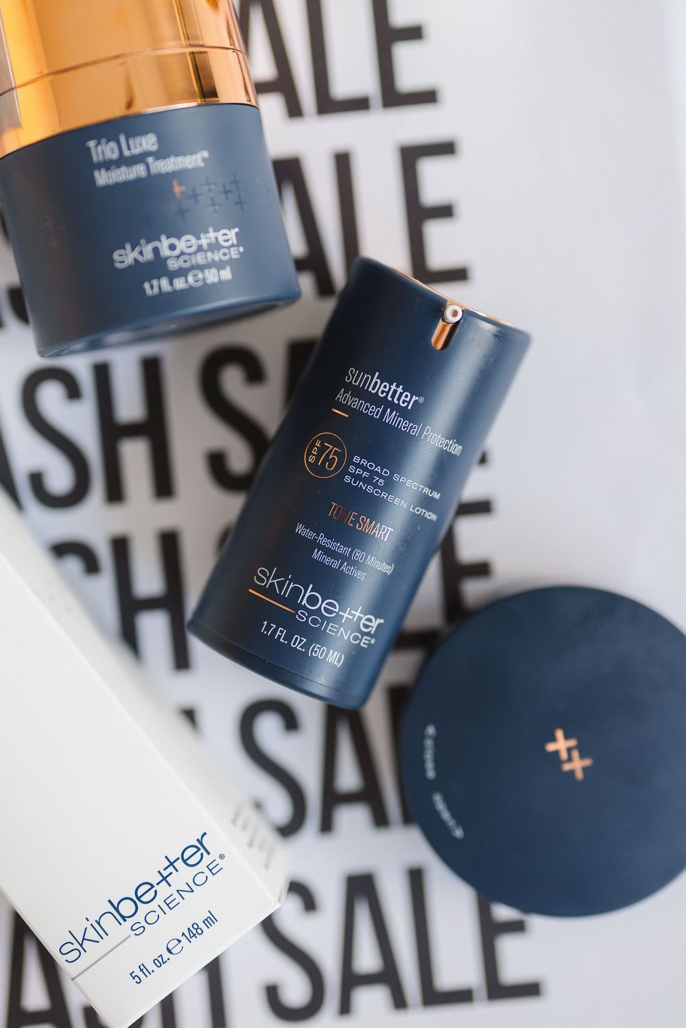 Skinbetter skincare products and containers arranged against a black and white sale sign background.