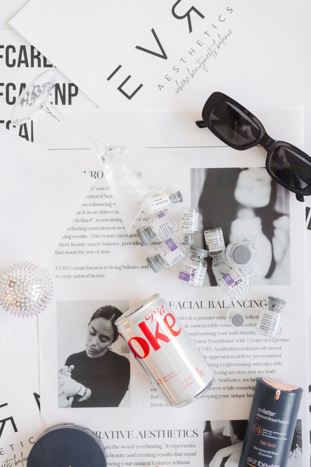 Flatlay with a Diet Coke can, sunglasses, beauty products and magazine clippings on a white surface.