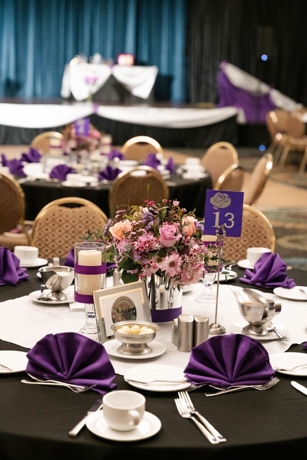 Elegant wedding reception tables with black tablecloths, purple napkins, and pink floral centerpieces set for formal dining.