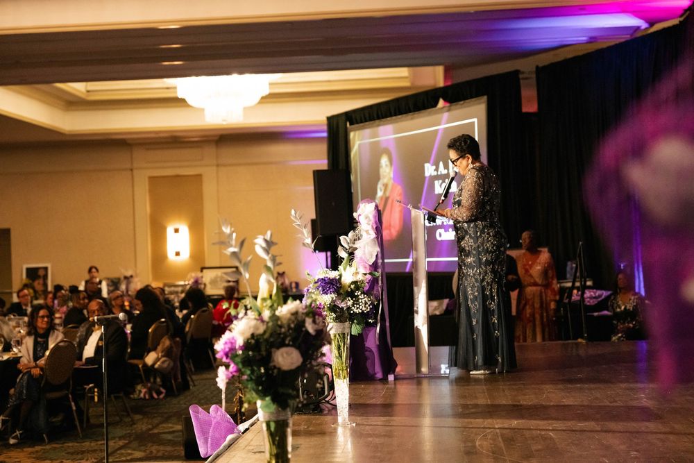 A celebration at a wedding reception venue with purple lighting and multiple guests seated at round tables.