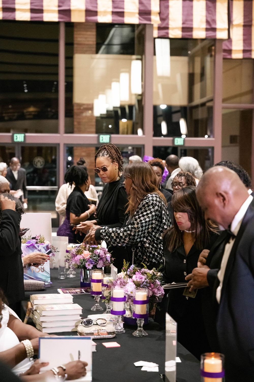 Event attendees gather at a table decorated with purple candles and floral centerpieces at an elegant indoor venue.