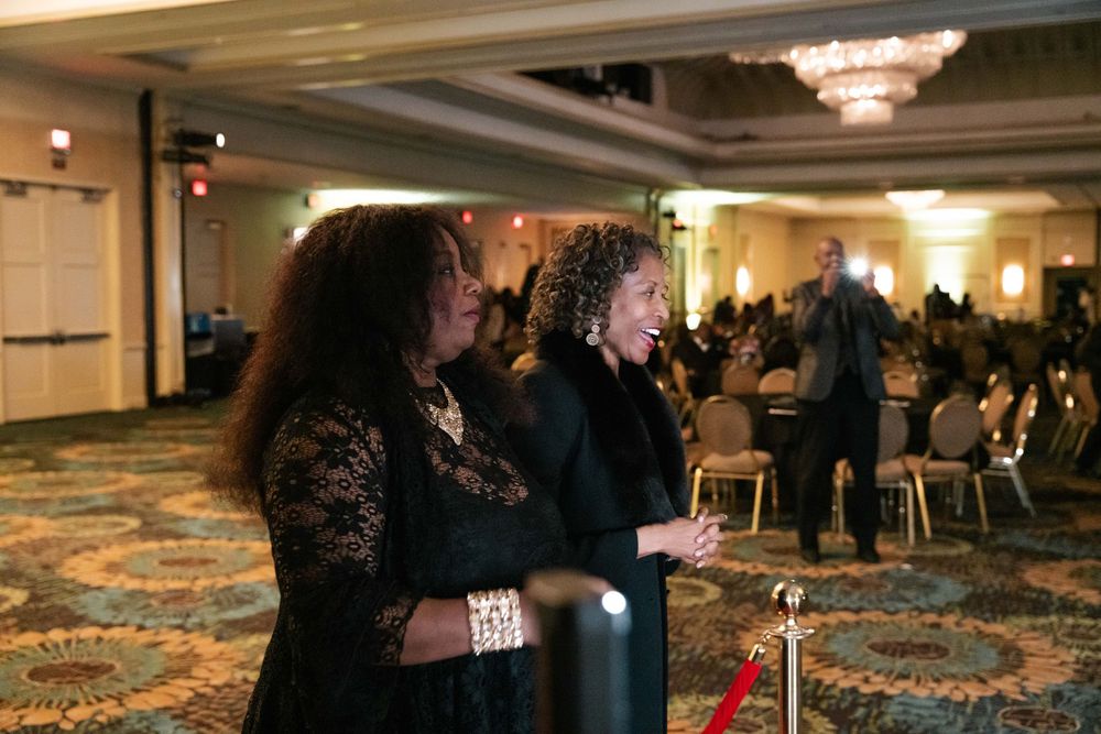 Two attendees react emotionally during an indoor event in an elegant hotel ballroom with carpeted floors.
