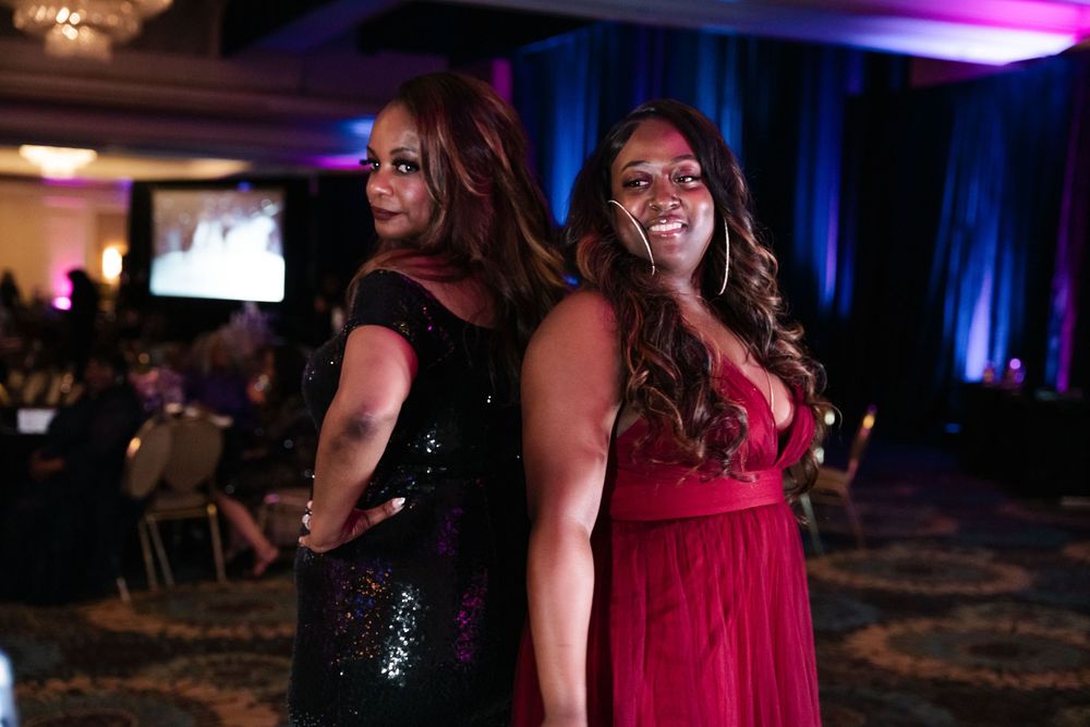 A festive group dances at an elegant evening event with purple and blue lighting in a hotel ballroom.