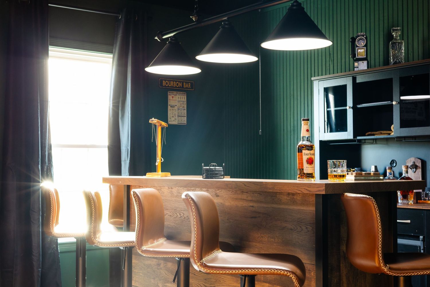 Modern bar interior with brown leather barstools and green walls illuminated by pendant lights and natural window light.