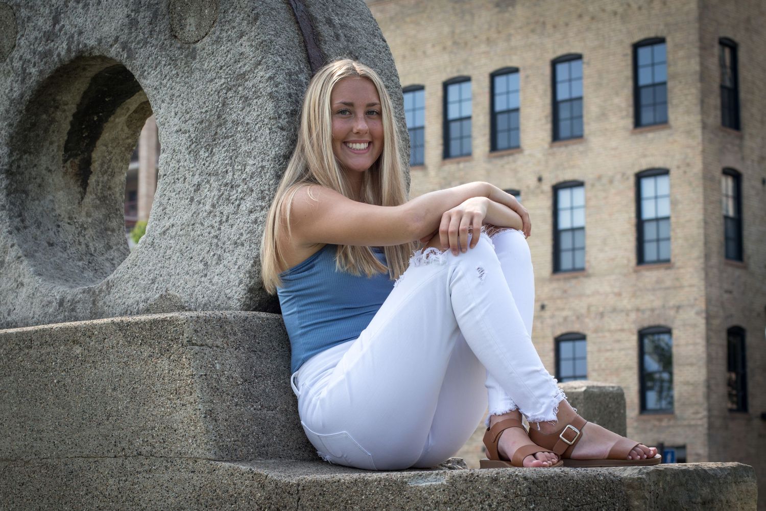 portrait of young lady sitting on a decorative cement monument with her ankles crossed