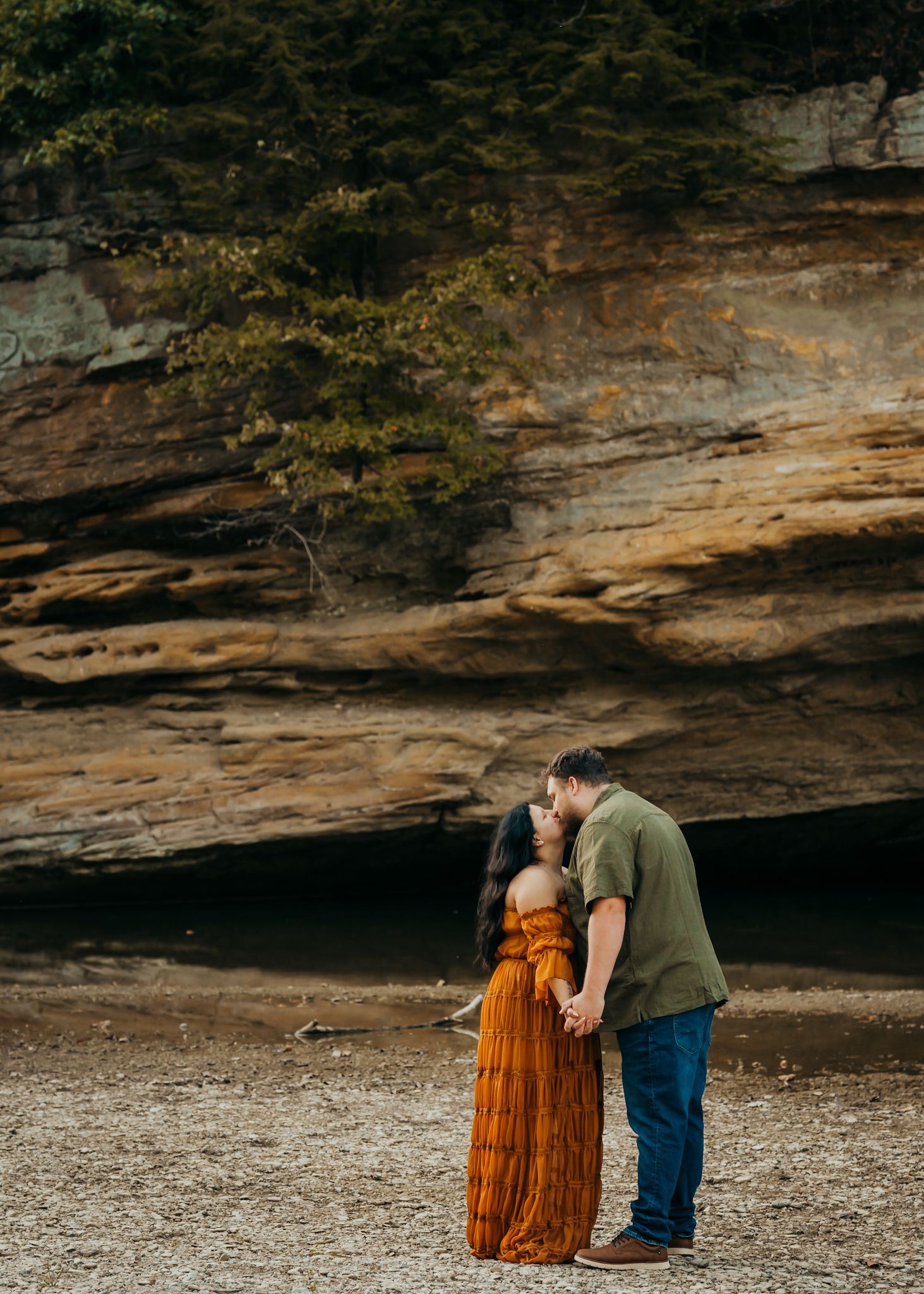 Couple kiss during portrait session in front of rock formation at Turkey Run State Park.