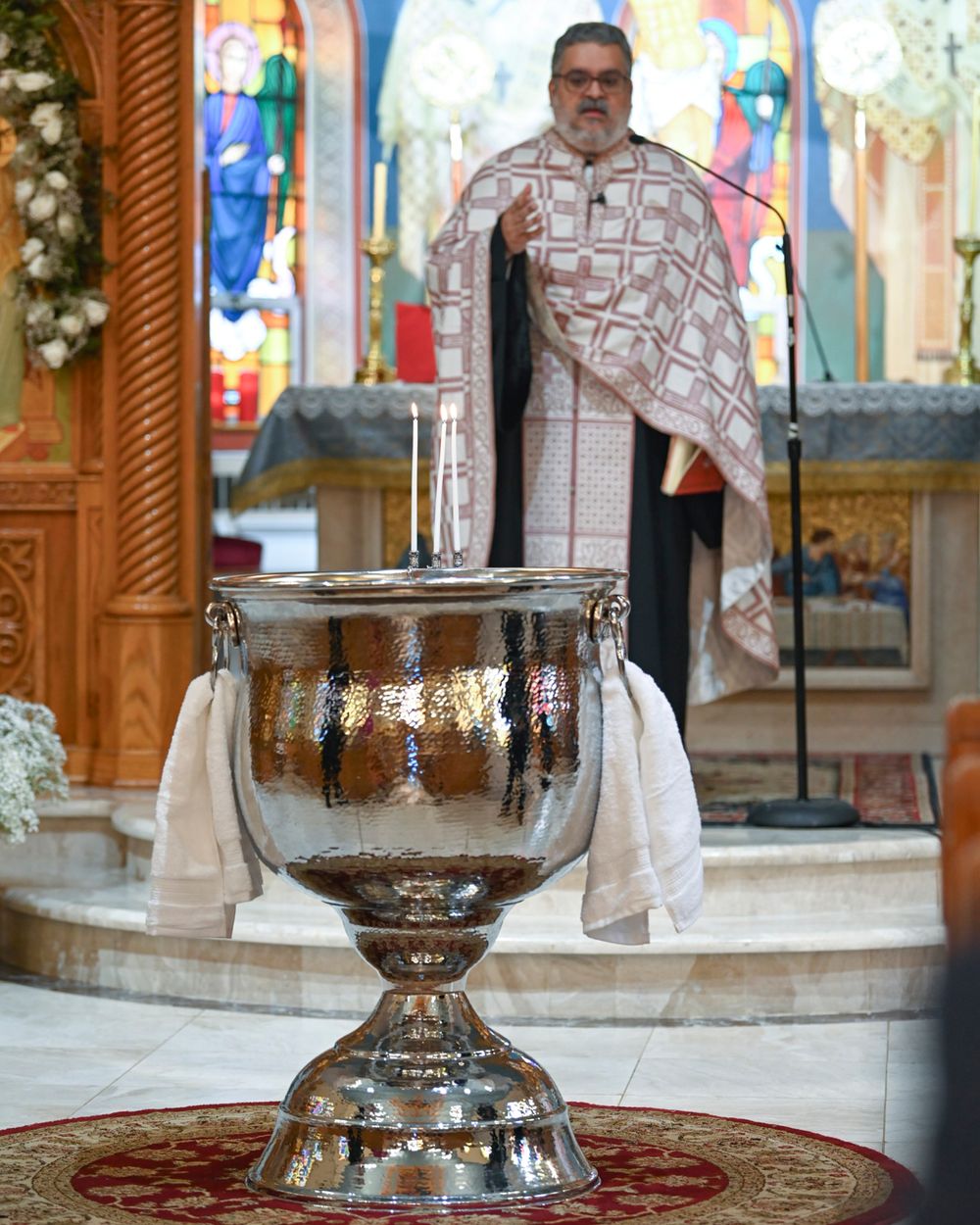Priest in ceremonial robes standing at altar near large baptismal font.