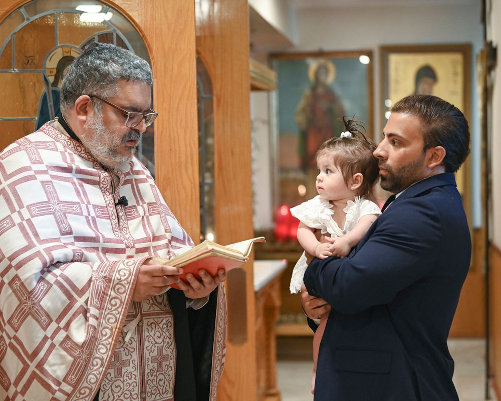 Orthodox priest reads from religious text during baptism ceremony in church with small infant.