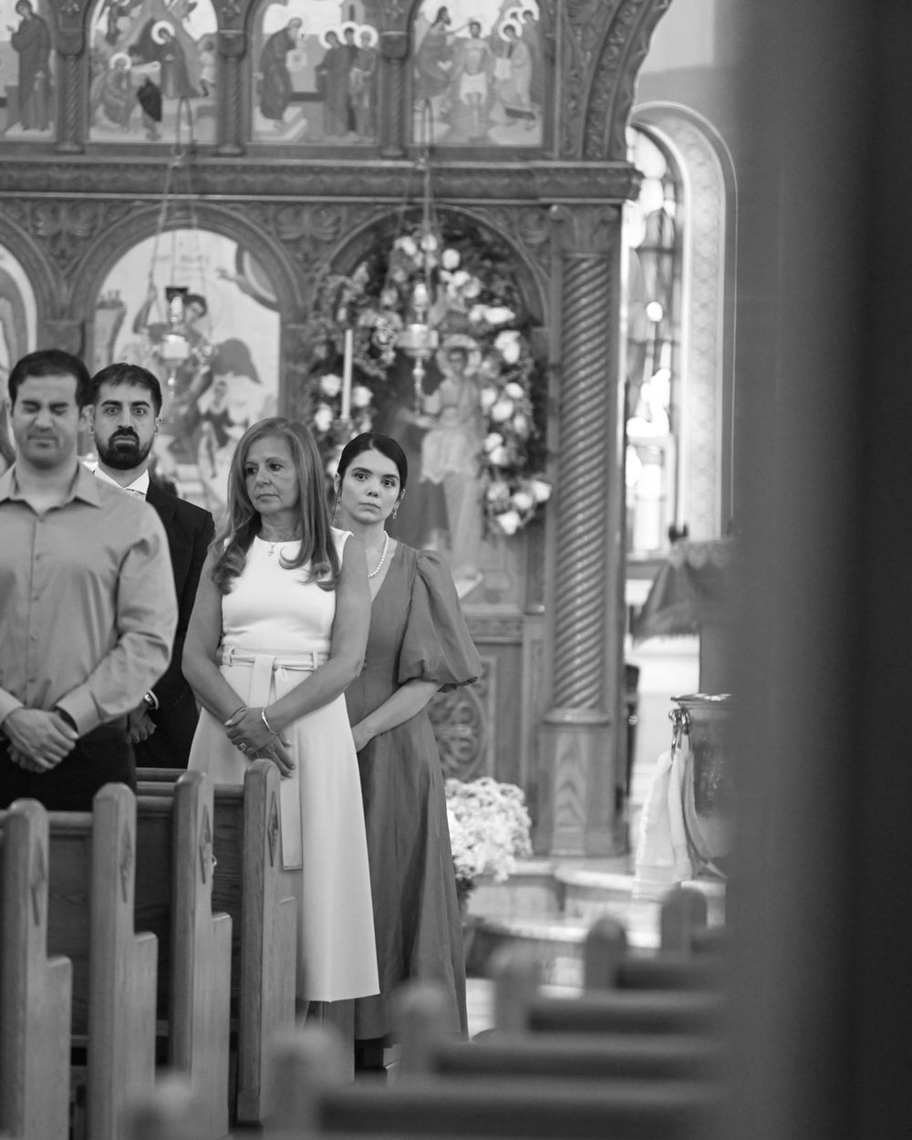 Black and white photo of people standing in church pews during ceremony.