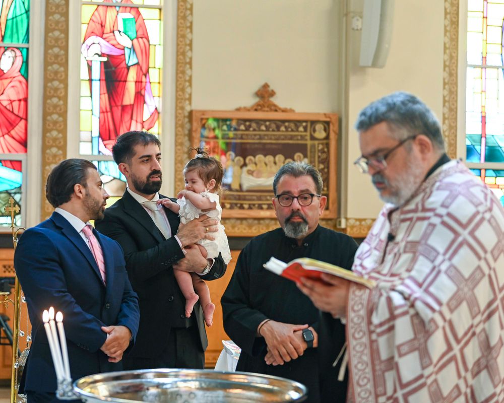 Religious baptism ceremony taking place in church with ornate stained glass windows.