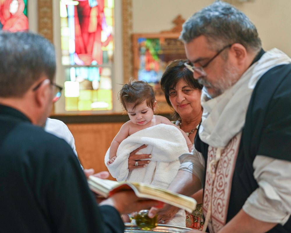 Baptismal ceremony in progress with priest and family gathered around infant.