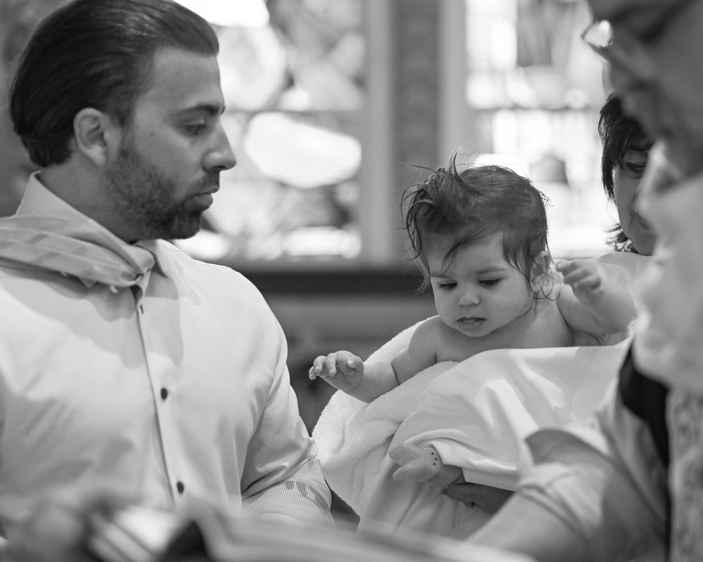 Black and white photo of infant baptism ceremony with family members.