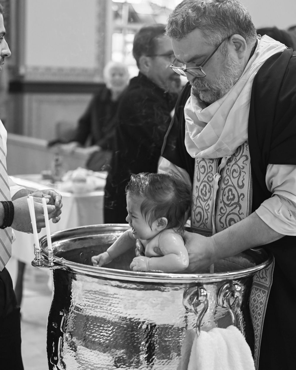 Priest performing baptism ritual with infant at silver baptismal font.