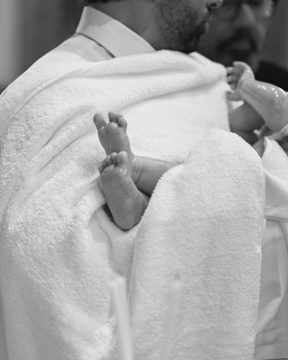 Tiny baby feet wrapped in white baptismal towel during ceremony.