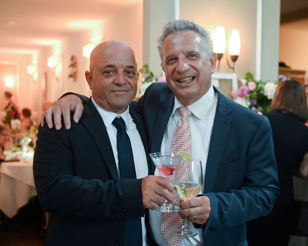 Two guests share a celebratory moment with champagne glasses at an indoor reception.