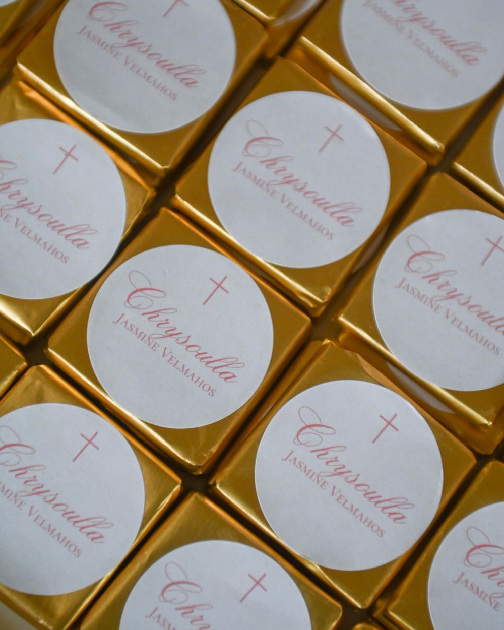 Gold-wrapped christening favors with white circular labels featuring crosses arranged in rows.
