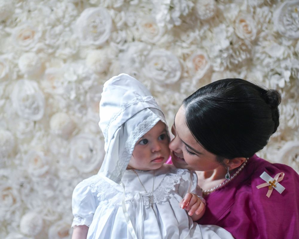 A tender moment captured against a floral backdrop at a christening ceremony.