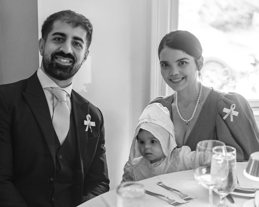 A formal celebration at a dining table with guests in elegant attire and a child in white.