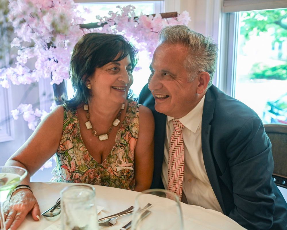 A couple sharing a joyful moment at a formal dining event with pink floral decorations.