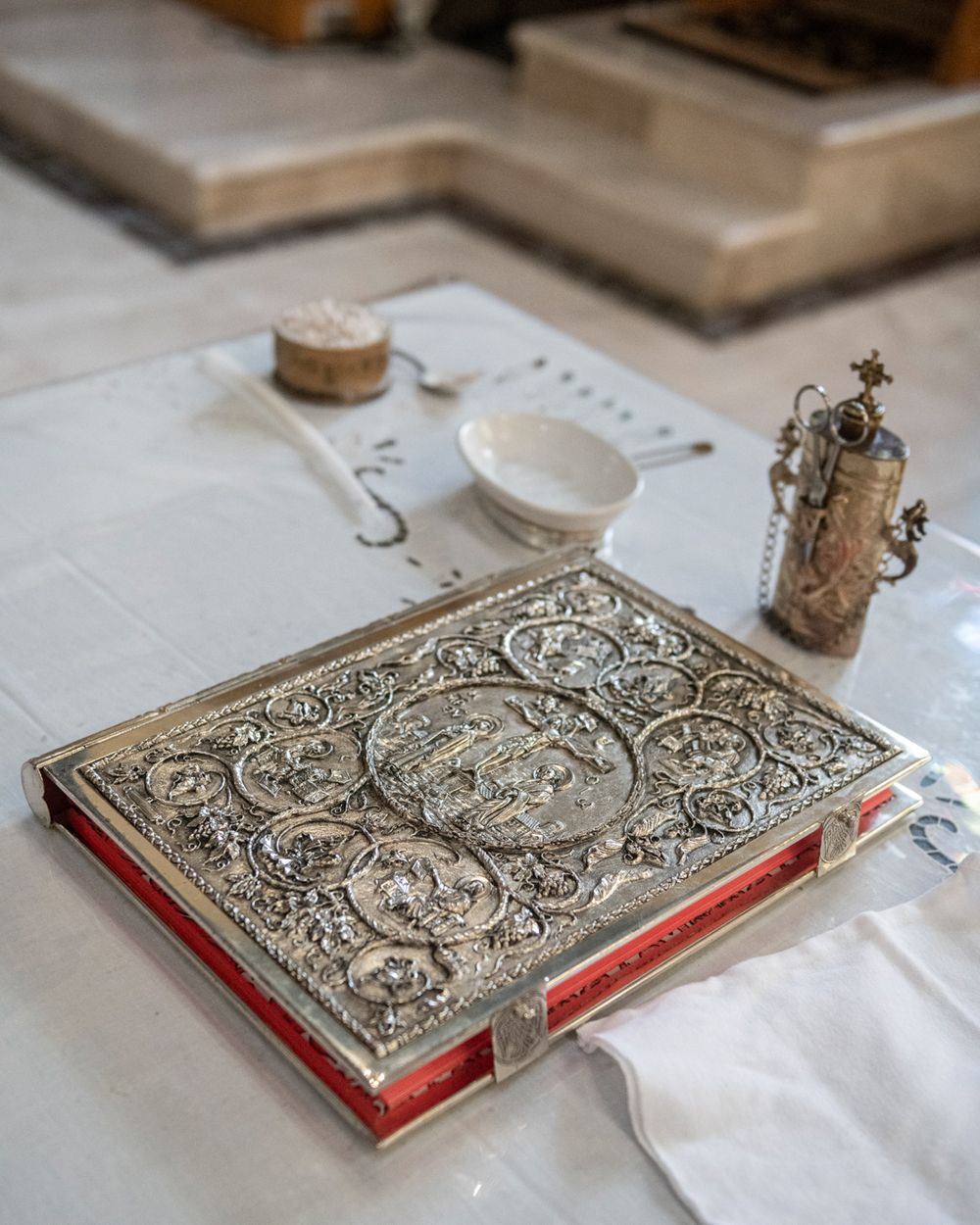 An ornate silver-embossed book with decorative details on a white tablecloth.