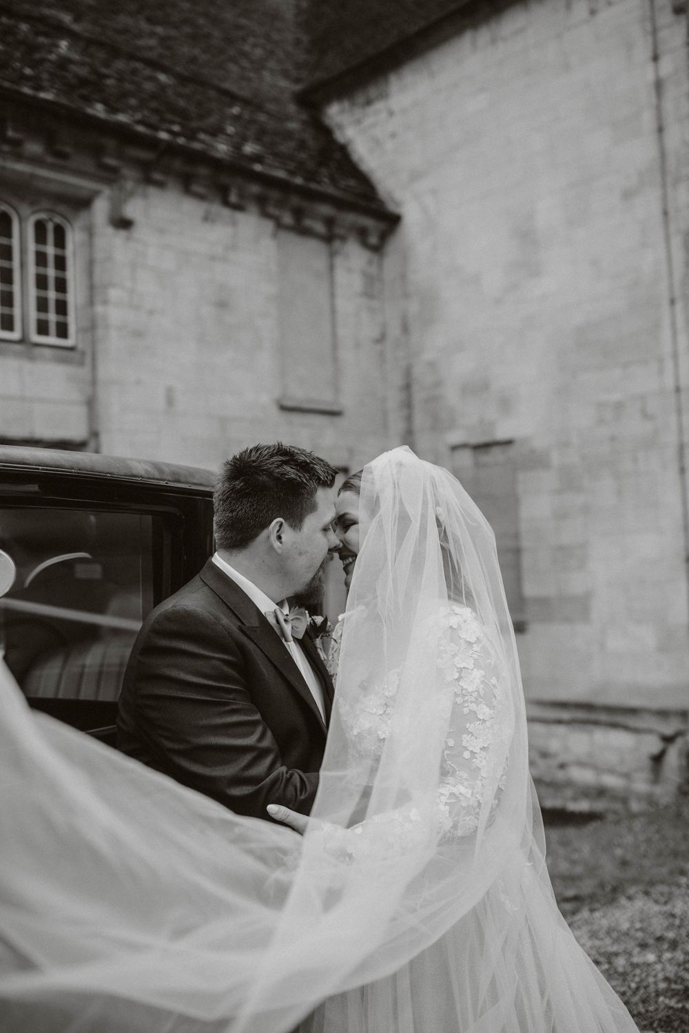 Black and white wedding photo with flowing veil against stone building backdrop. Blackfriars priory