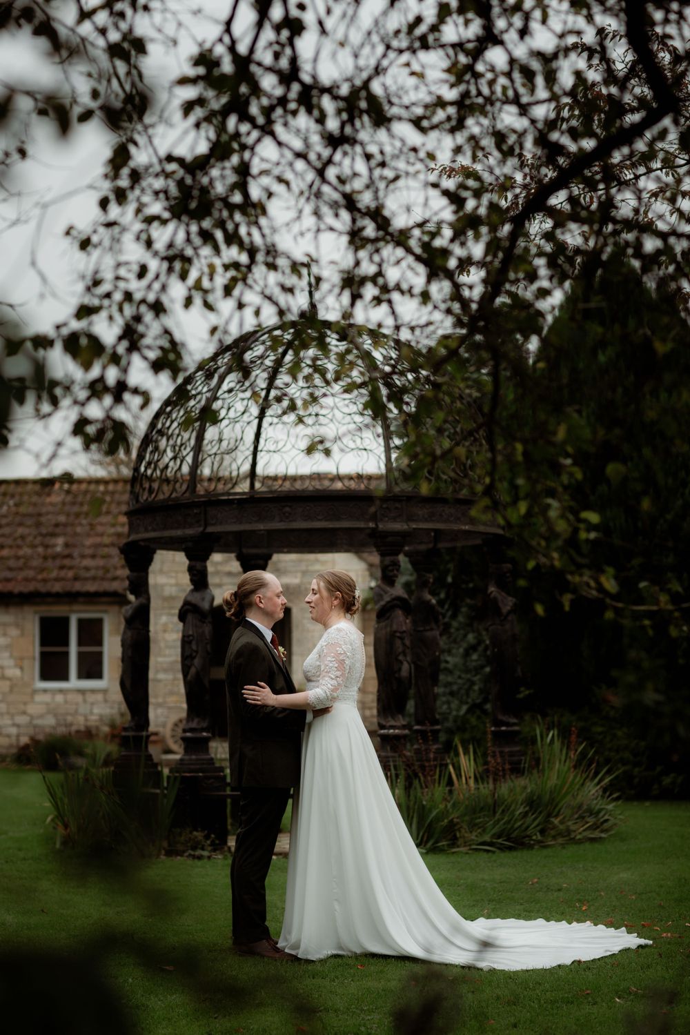Wedding couple standing under an ornate garden gazebo in a lush green setting. Widbrook grange marriage