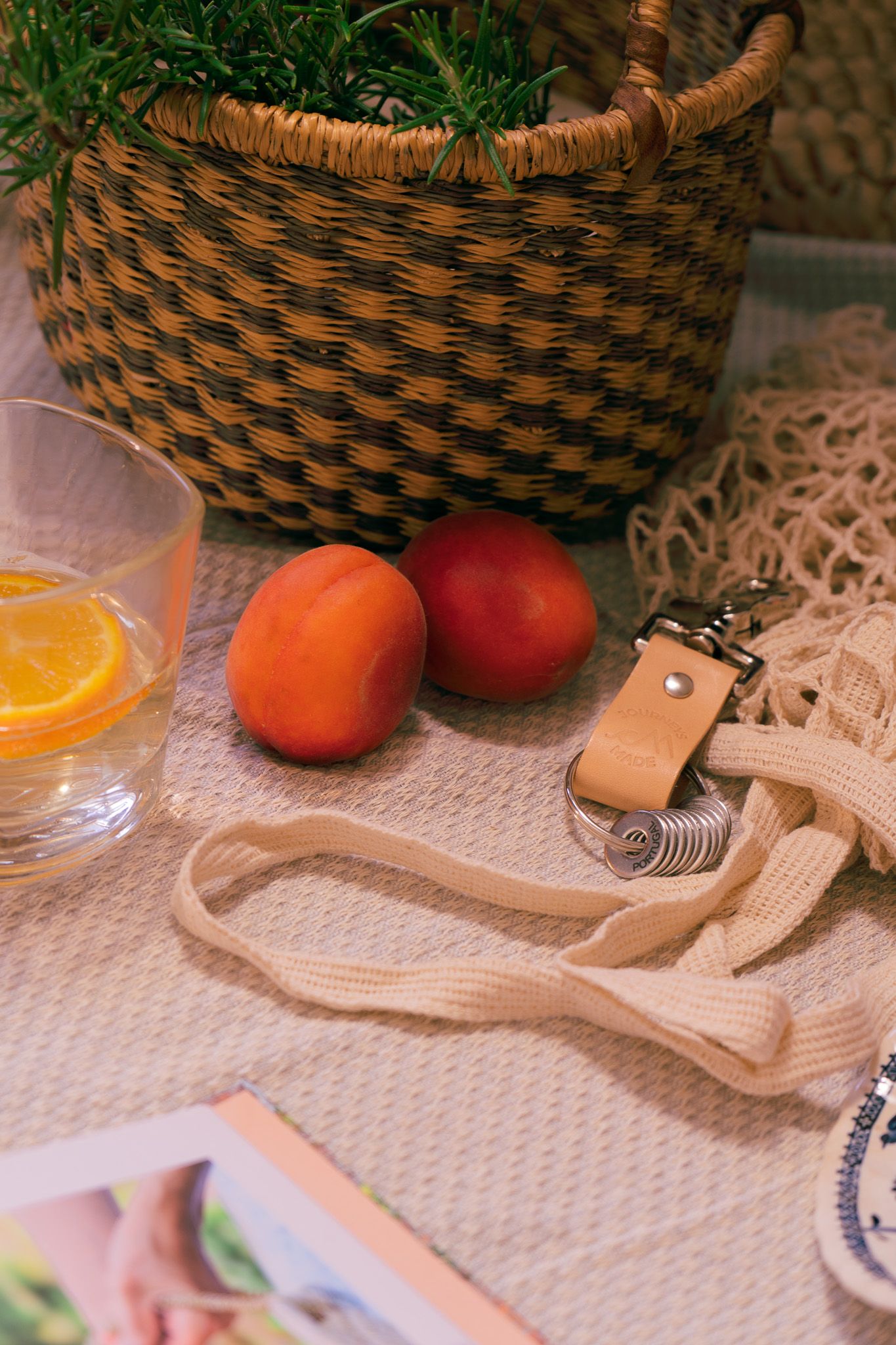 lifestyle photo of travel keyring amongst a basket of herbs, a book and pottery,  shopping bag, warm summery aesthetic