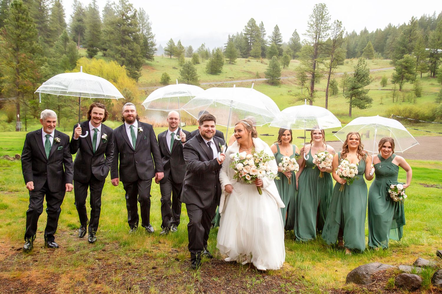 A rainy day wedding in Cle Elum, Washington. A beautiful bride, groom, and wedding party walk toward the camera holding umbrellas.