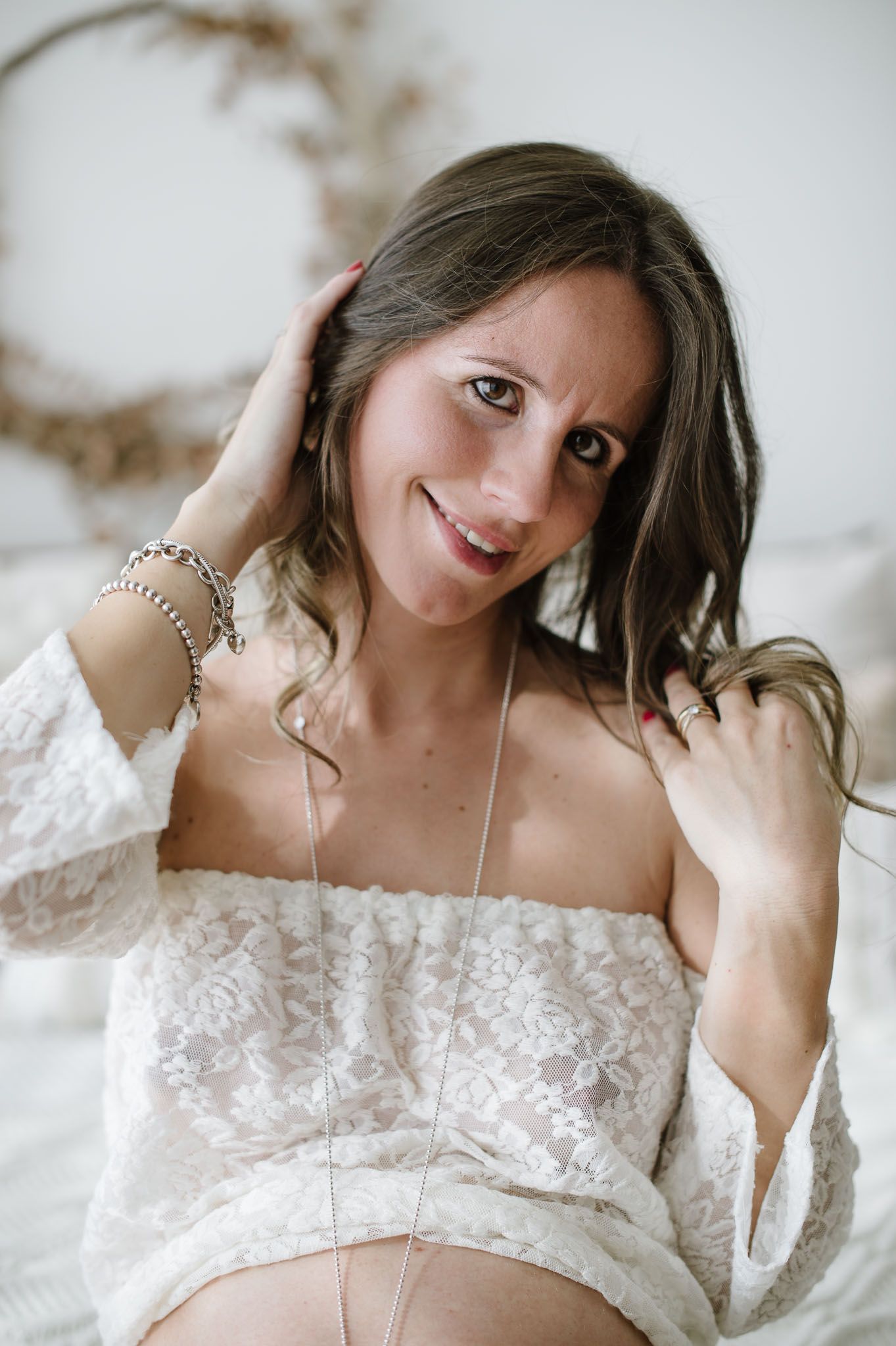 A romantic maternity photo of an expectant mother wearing an off-shoulder white lace dress.