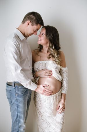 Intimate moment between expectant parents as they embrace against white wall.