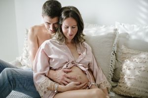 Intimate maternity photo of couple embracing on white couch with decorative pillows.