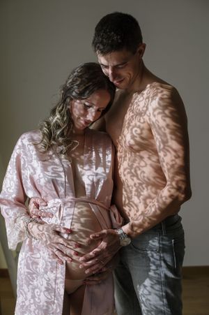 Romantic maternity portrait with natural window light creating shadow patterns.