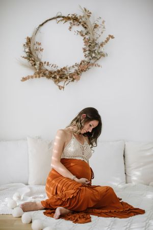 Maternity portrait with dried floral wreath decor and rust-colored dress on white couch.