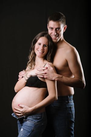 Intimate maternity portrait of expecting couple against dark background.