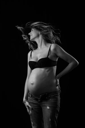 Black and white portrait of pregnant woman in jeans with windswept hair.
