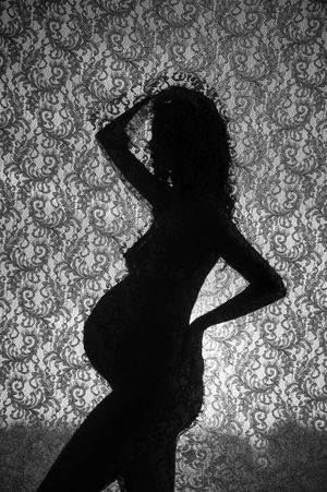 Dramatic silhouette of pregnant figure against ornate lace background pattern.
