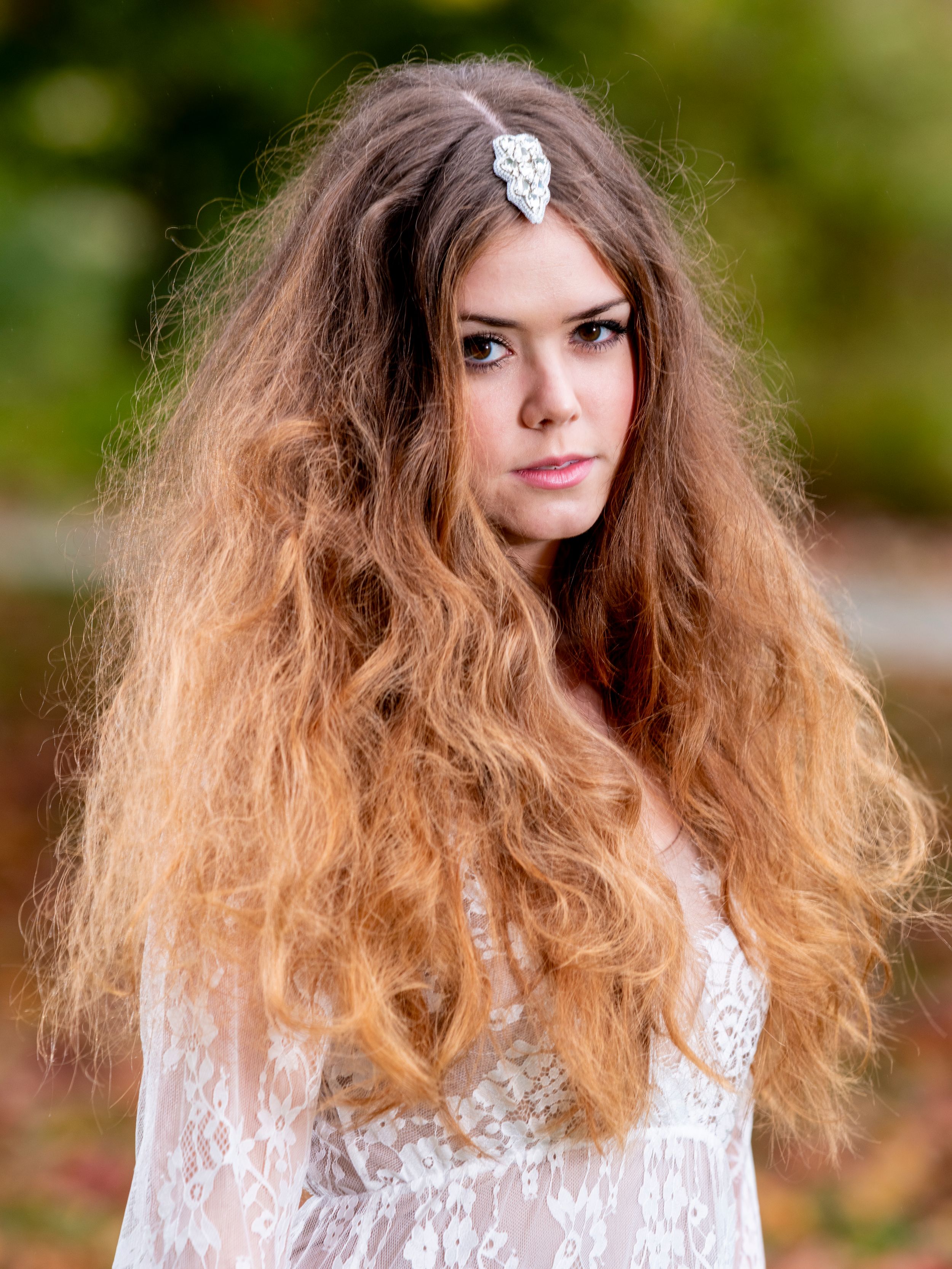Long wavy blonde ombre hair and white lace dress in outdoor portrait with natural bokeh background.