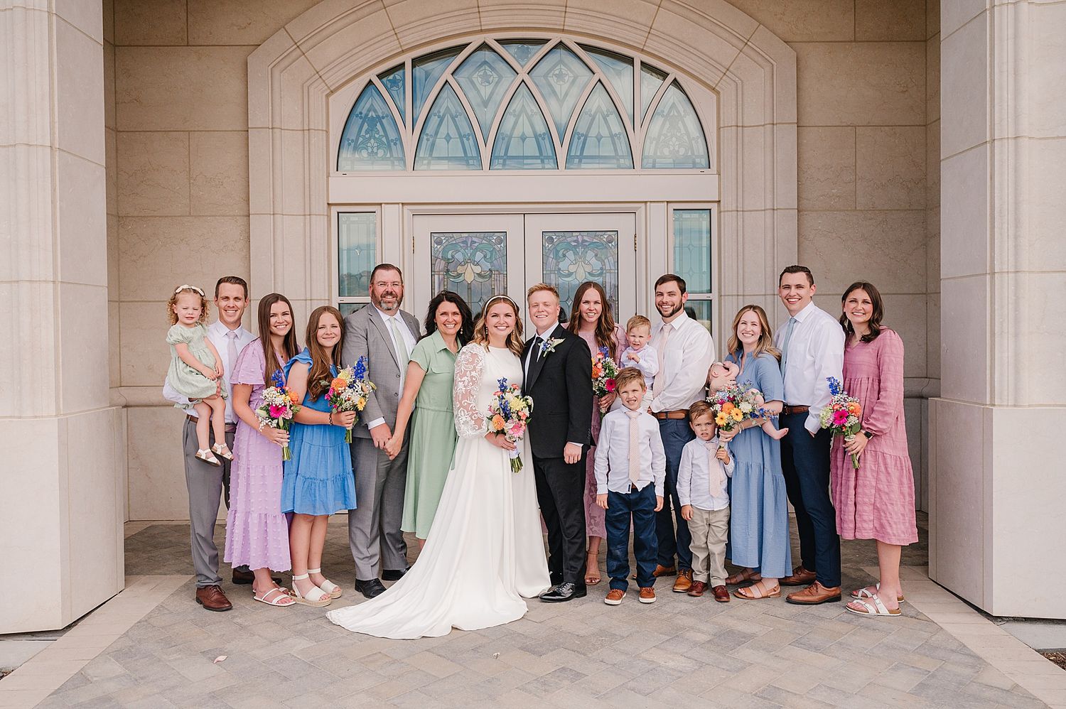 Wedding party poses together under an elegant arched doorway with decorative windows at a church venue.