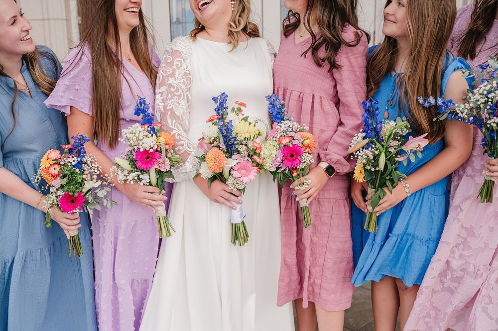 Close-up of bridal party holding colorful floral bouquets in pink and blue pastel dresses.