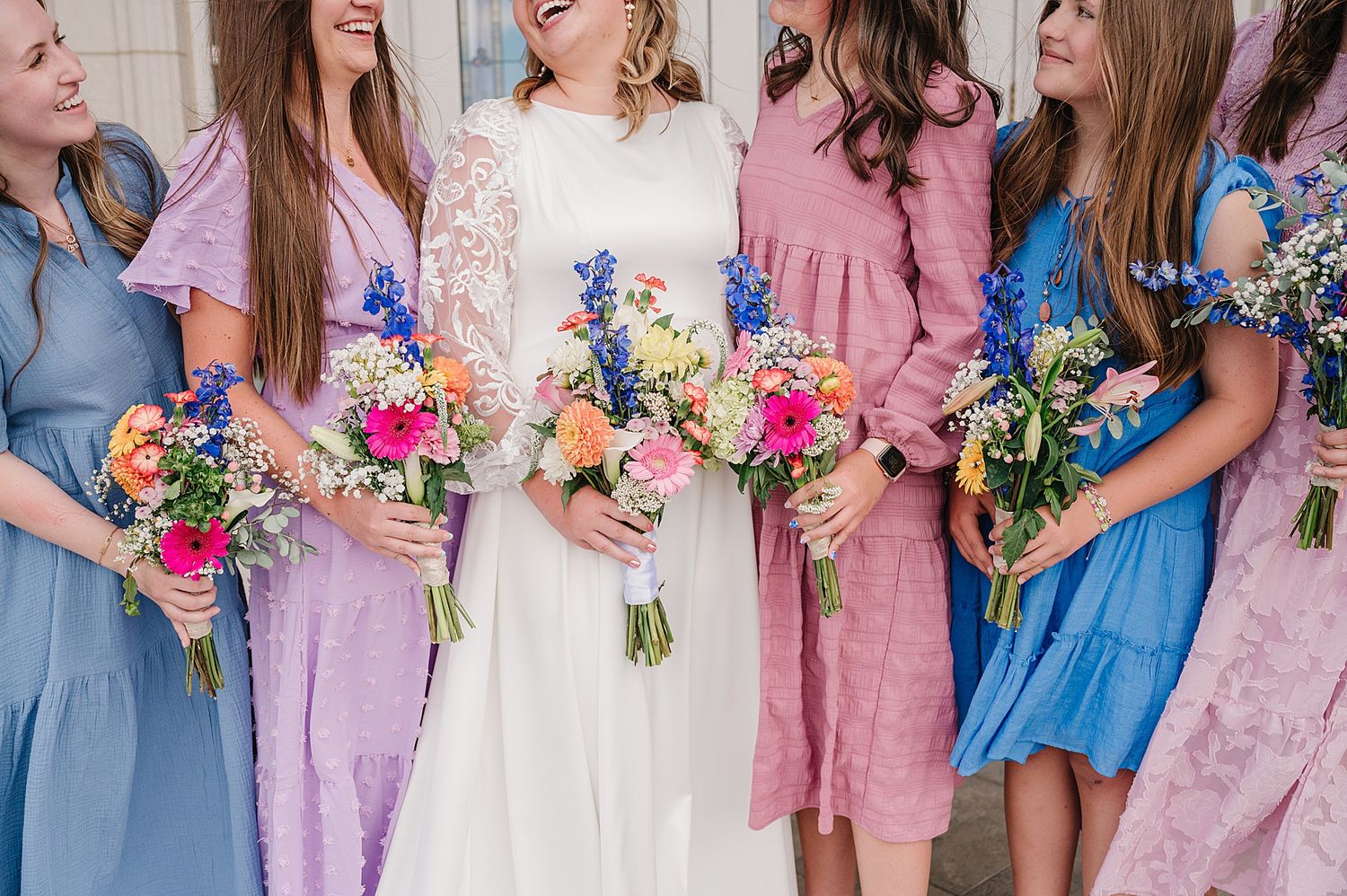 Close-up of bridal party holding colorful floral bouquets in pink and blue pastel dresses.