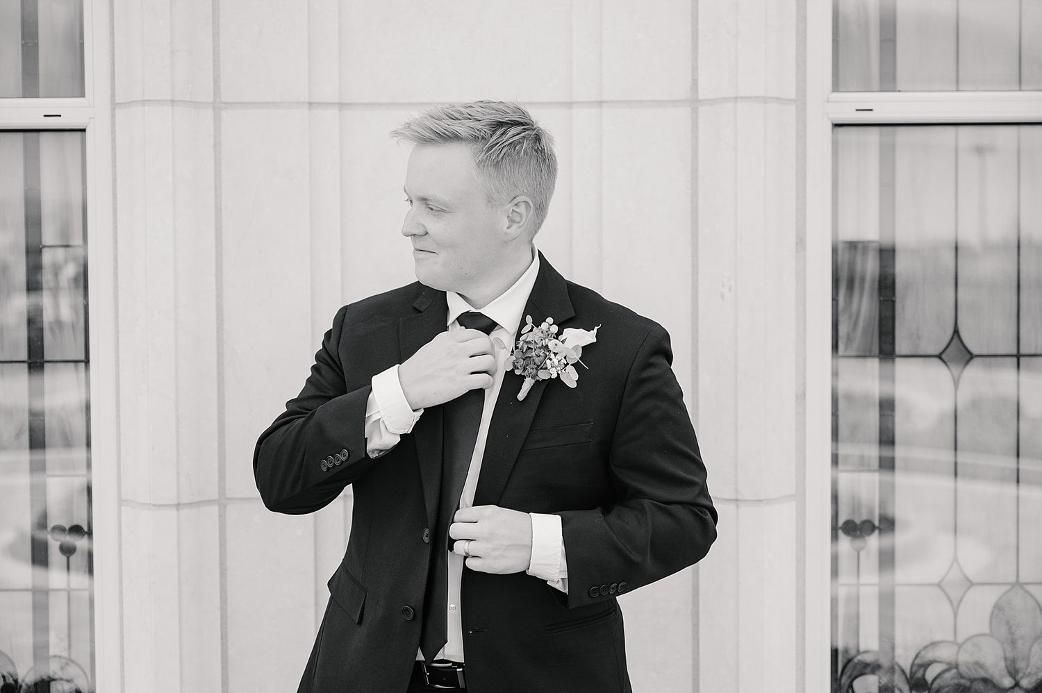 Black and white portrait of groom adjusting bowtie while wearing classic tuxedo.