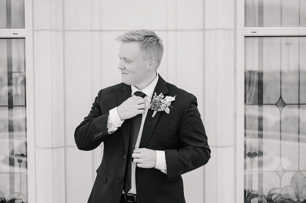 Black and white portrait of groom adjusting bowtie while wearing classic tuxedo.