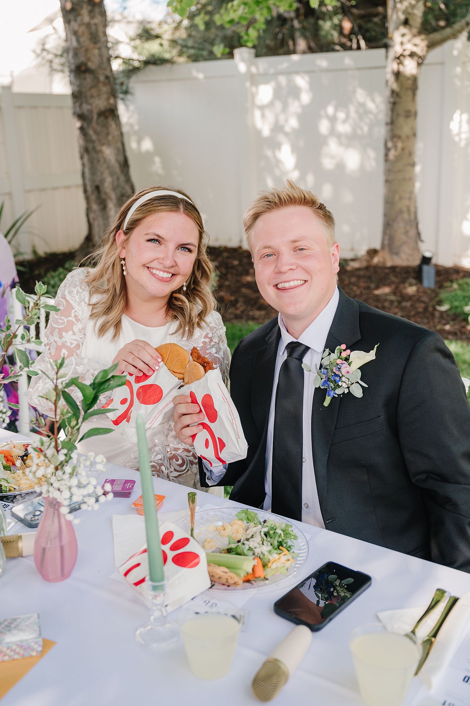 A couple shares a joyful moment at an outdoor reception table decorated with floral arrangements and pink drinks.