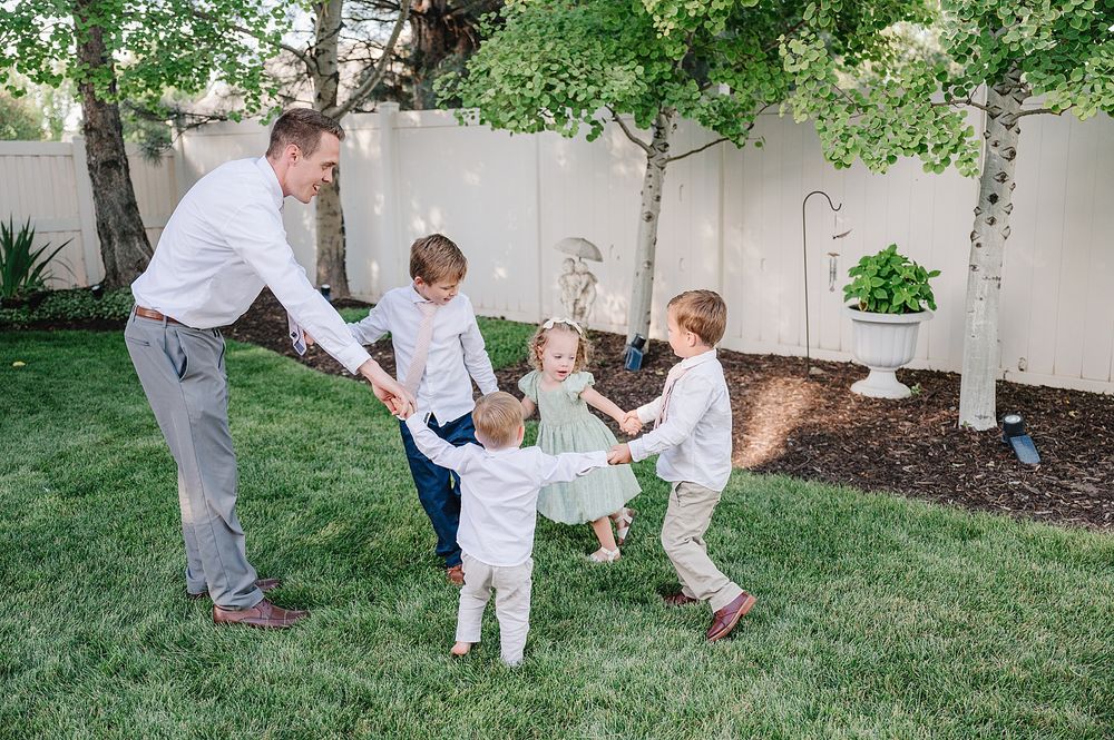 People enjoying playful activity on a grassy lawn with landscaped backyard and white fence in the background.