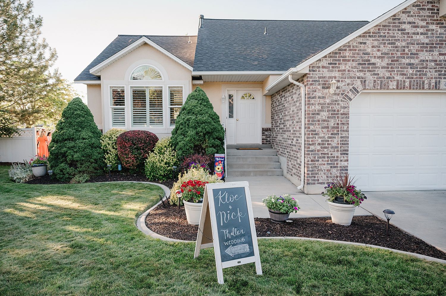 A charming brick house with neat landscaping and a white welcome sign on the manicured lawn.