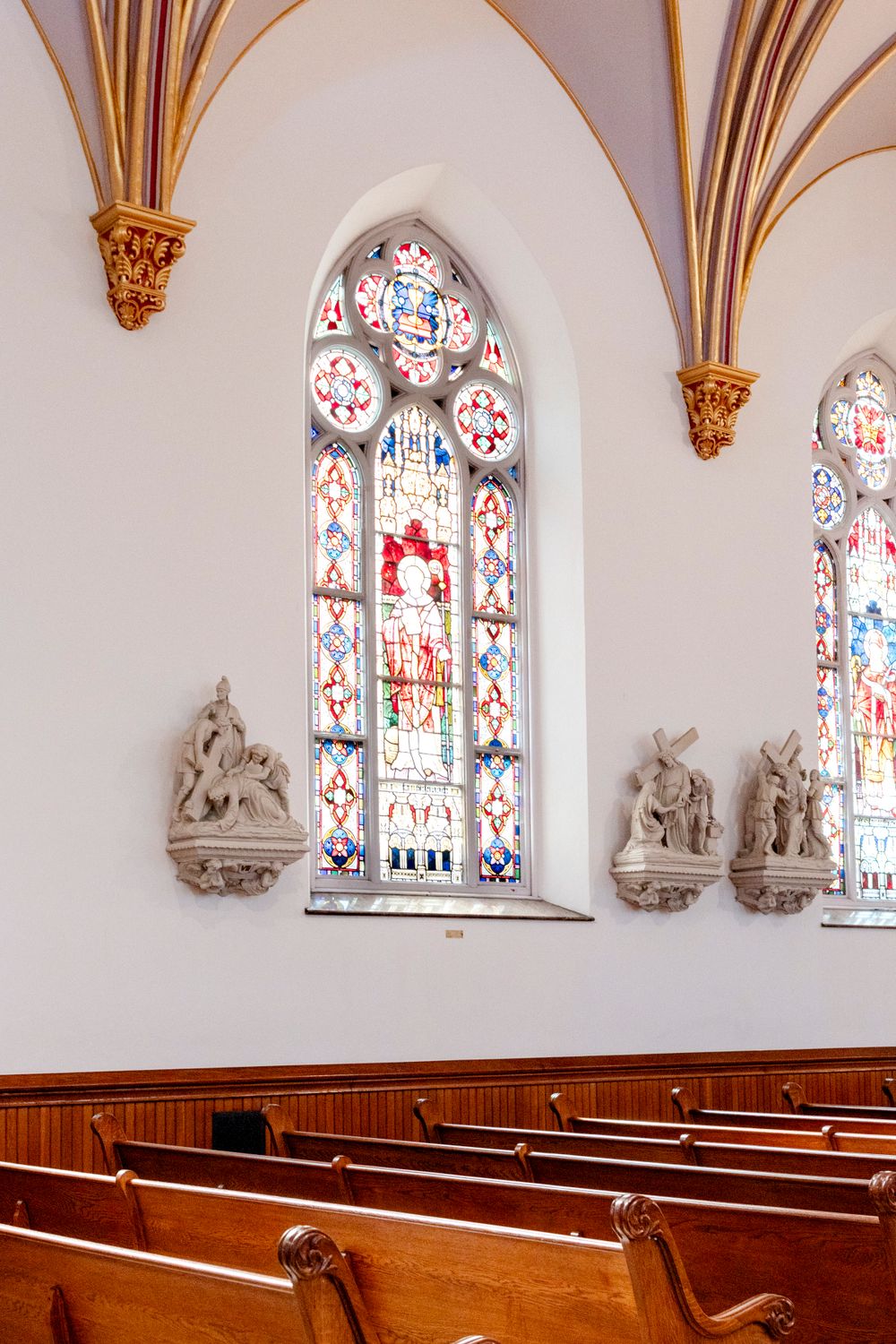 Interior of church with stained glass windows, wooden pews, and decorative architectural details.