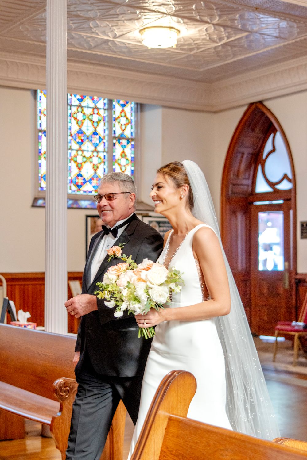 Elegant church interior featuring stained glass windows and ornate ceiling details during a wedding processional.